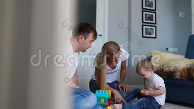 幸福的家庭爸爸妈妈和宝宝在他们明亮的客厅里玩乐高。 慢镜头拍摄幸福家庭